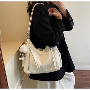 Detail of a creamy white pleated shoulder bag with long tassels and cloud plush charm