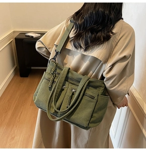 Model wearing a large army green corduroy tote bag with multiple zip pockets and straps