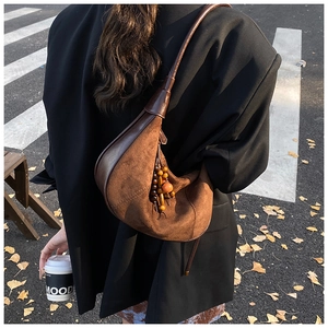 Detail of dark brown suede crescent shoulder bag with wooden beaded fringe on black blazer