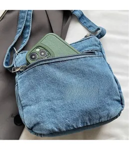 Detailed view of the back zipper pocket on a blue denim crossbody bag with a mobile phone