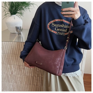 Detail of burgundy matte leather crossbody bag featuring an adjustable strap and metal logo