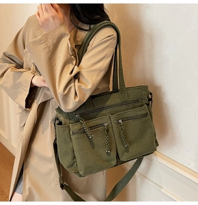 Detail of corduroy tote bag in army green featuring two front zippered pockets on model
