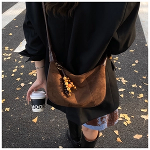 Detail of dark brown suede crescent bag with beaded tassel in a leafy autumn street setting
