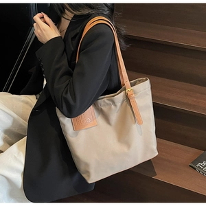 Close-up of a large khaki canvas tote bag with brown leather straps and metal buckle