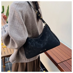 Model wearing a black suede crescent underarm bag with gold logo in a garden setting