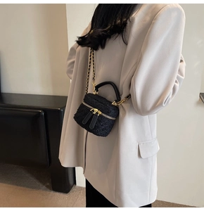 Detail of black tweed mini bag showing woven texture and gold chain strap on grey blazer