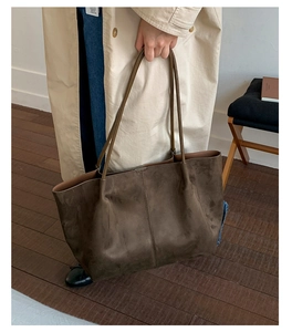 Detail view of large dark brown matte leather tote bag worn with a casual trench coat