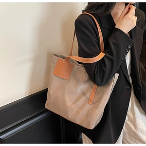 Detail of khaki tote bag with brown leather handles worn by a model in a black suit
