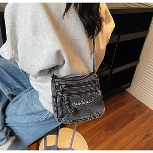 Detail of dark grey vintage denim crossbody bag with multiple zippers and embroidery