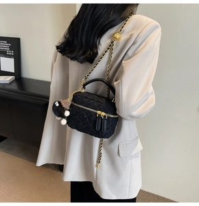 Close-up of black tweed crossbody box bag with gold chain and plush charm on white blazer