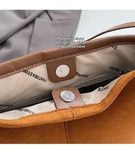Gros plan sur le fermoir magnétique et la poche zippée d'un sac cabas en daim marron