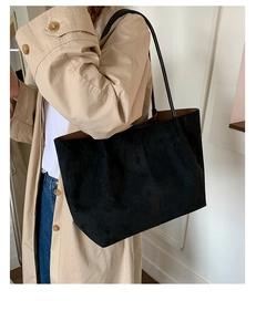 Close-up of minimalist black suede tote bag styled with a khaki trench coat for office wear