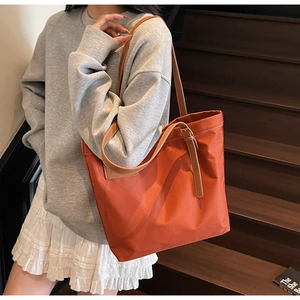 Detail of orange nylon tote bag showing brown leather straps and metal buckle accents