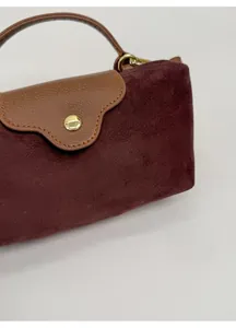 Close-up of burgundy suede bag featuring brown leather flap and golden snap closure