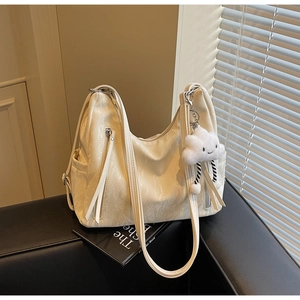 Detail of cream leather tote bag with soft texture and cloud plush charm on a sofa