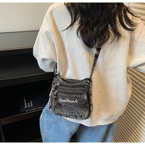 Detail of washed black denim crossbody bag featuring multi-pocket zippers and embroidery