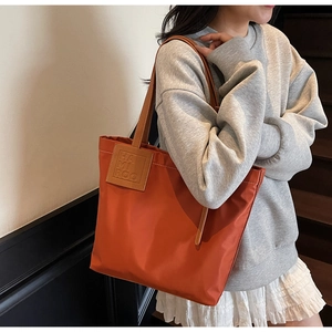 Detail shot of the orange nylon tote bag with leather straps on a fashion model