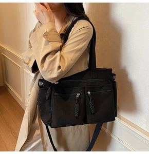 Detail view of black corduroy tote bag showing front zipper pockets and woven rope pullers