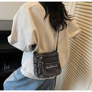 Detail view of black washed denim crossbody bag with three zipper pockets and embroidery