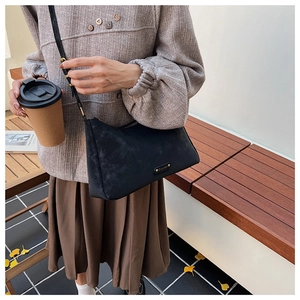 Detail of a vintage black frosted leather crossbody bag with a gold metal brand plaque