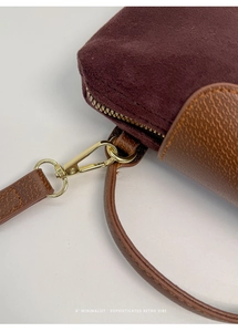 Close-up of retro burgundy suede bag with brown leather trim and gold metal hardware