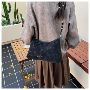 Close-up of black retro hobo bag with matte texture and metallic logo on a person