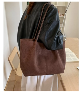 Detail of a large dark brown suede tote bag carried by a model in a minimalist room