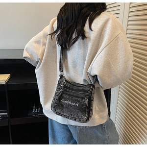 Detail of grey washed denim crossbody bag with multiple zippers and logo embroidery