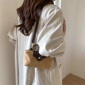 Detail view of mustard yellow suede crossbody bag with brown leather strap on a model