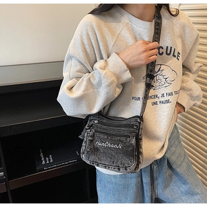 Detail of black washed denim crossbody bag with white embroidery and multi-pocket design