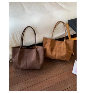 Detail of minimalist suede tote bags in dark brown and camel on a wooden floor