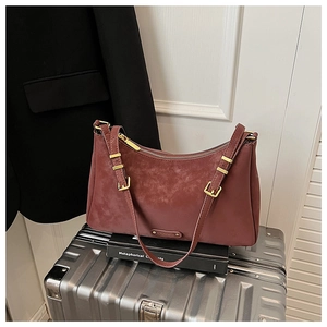 Detail of burgundy matte shoulder bag with gold hardware and zipper on silver suitcase
