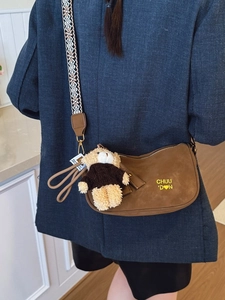 Sac bandoulière demi-lune marron avec sangle brodée et charm ours porté par un mannequin