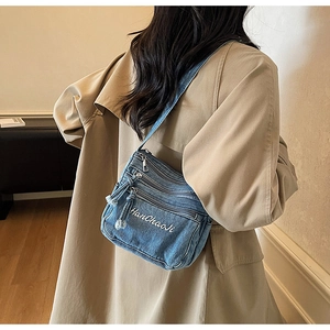 Blue denim crossbody bag featuring multiple zipper pockets and white embroidery detail