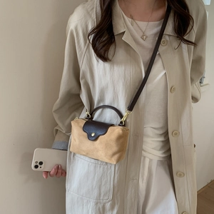 Detail of suede crossbody bag showing the contrast leather flap and gold hardware