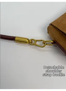 Detail of matte gold metal clasp and detachable burgundy rope strap on brown suede bag
