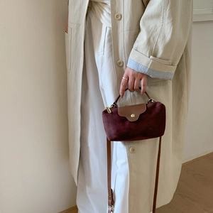 Detail of burgundy suede handbag featuring brown leather flap and golden round buckle