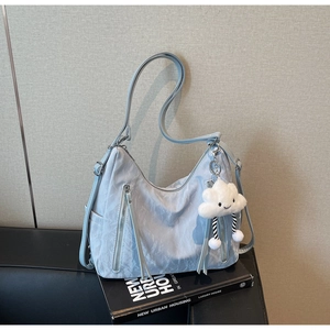 Detail of light blue textured tote bag with cloud charm and vertical zippers on a book