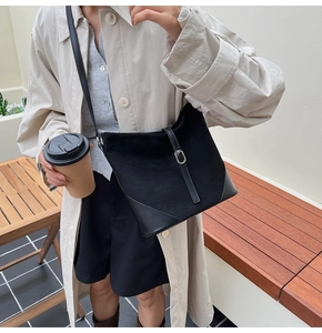 Détail du sac seau noir en daim et cuir porté par un mannequin dans un décor de ville chic