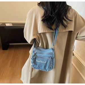 Detail of blue denim crossbody bag featuring white embroidery and vintage wash texture