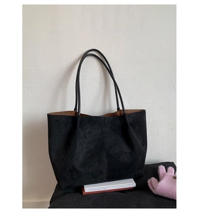 Detail of a large black faux suede tote bag with brown lining on a stool with books