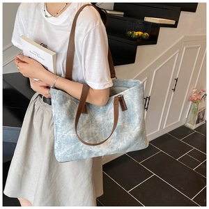 Detail of light blue textured tote bag with dark brown leather straps and metal logo