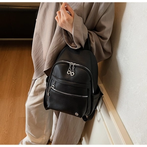 Close-up of black lychee leather backpack showing silver zippers and textured material
