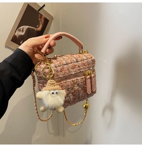 Close-up of pink tweed mini handbag featuring gold chain strap and plush white charm