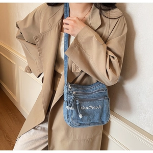 Detail of light blue denim crossbody bag featuring multi-layer zipper pockets and embroidery