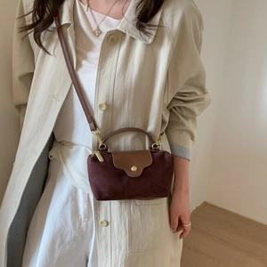 Detail of burgundy faux suede handbag with brown leather flap and golden hardware on trench coat