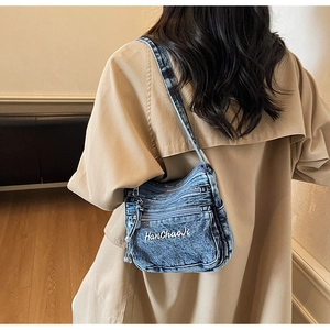 Detail of blue denim crossbody bag with multiple zippers and white letter embroidery