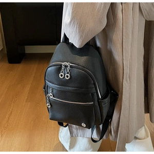 Detail of black lychee grain leather backpack with silver zippers on beige coat