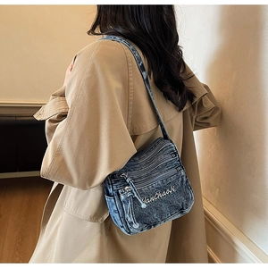 Blue denim crossbody bag with multi-zipper compartments worn by a model in a trench coat