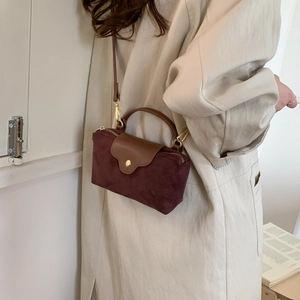 Detail of burgundy faux suede and brown leather crossbody bag held by a model